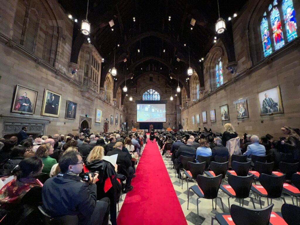 Guests seated for a formal event in a grand hall with a red carpet